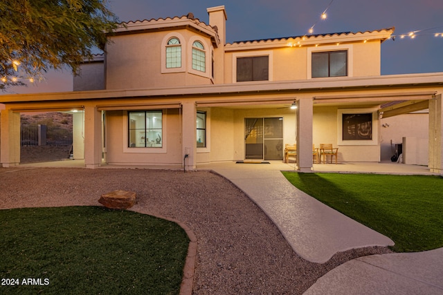 back house at dusk with a yard and a patio