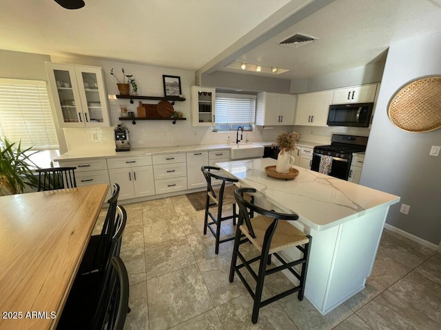 kitchen featuring white cabinets, black appliances, visible vents, and a breakfast bar