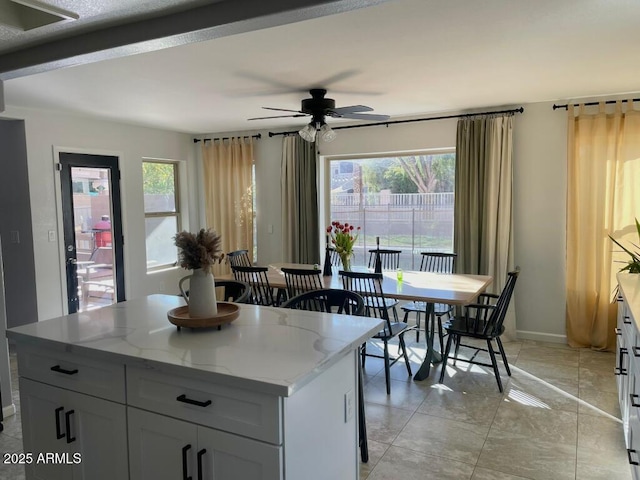 kitchen featuring plenty of natural light, a center island, a ceiling fan, and light stone countertops