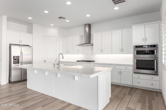 kitchen featuring stainless steel appliances, a kitchen island with sink, sink, and wall chimney range hood