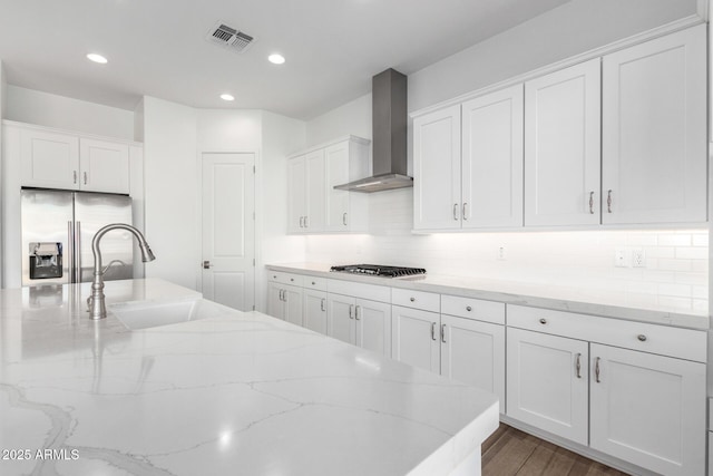 kitchen featuring wall chimney exhaust hood, sink, white cabinetry, stainless steel appliances, and light stone countertops