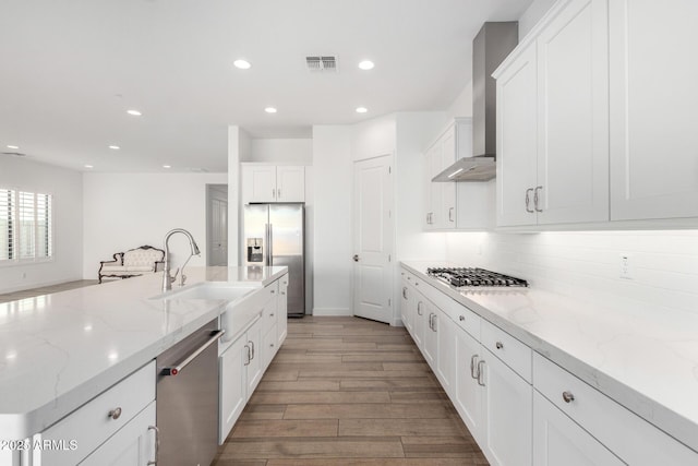 kitchen featuring sink, appliances with stainless steel finishes, wall chimney range hood, light stone countertops, and white cabinets