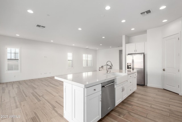 kitchen featuring sink, a kitchen island with sink, stainless steel appliances, light hardwood / wood-style floors, and white cabinets