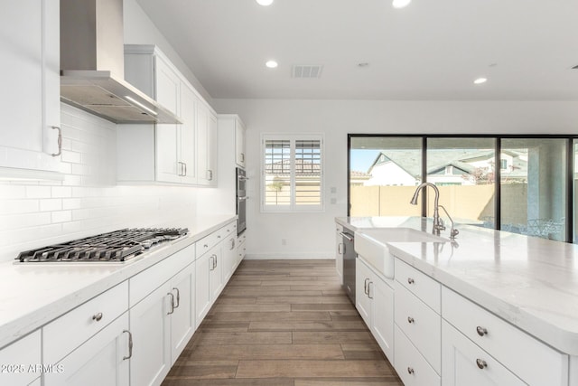 kitchen featuring appliances with stainless steel finishes, sink, backsplash, light stone counters, and wall chimney exhaust hood