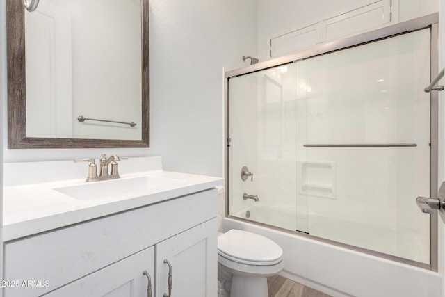 full bathroom with hardwood / wood-style flooring, vanity, shower / bath combination with glass door, and toilet