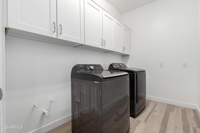 clothes washing area with cabinets, light hardwood / wood-style floors, and washer and dryer