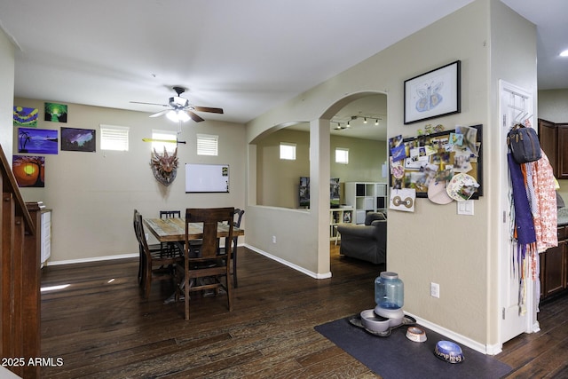 dining area featuring arched walkways, a ceiling fan, baseboards, and dark wood-type flooring