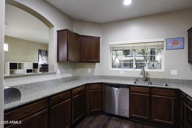 kitchen featuring arched walkways, stainless steel dishwasher, light stone countertops, a sink, and dark wood-type flooring