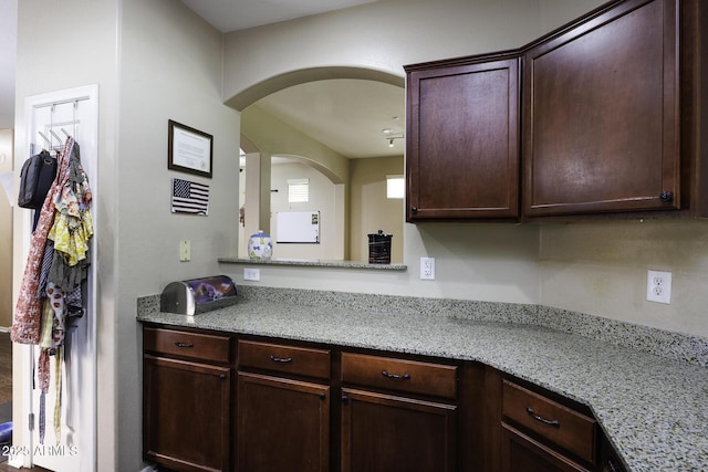 kitchen with arched walkways, dark brown cabinetry, and light stone countertops