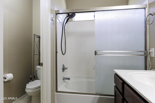 bathroom featuring vanity, enclosed tub / shower combo, a textured wall, and toilet