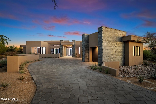 view of front of property featuring a garage, stone siding, decorative driveway, and stucco siding