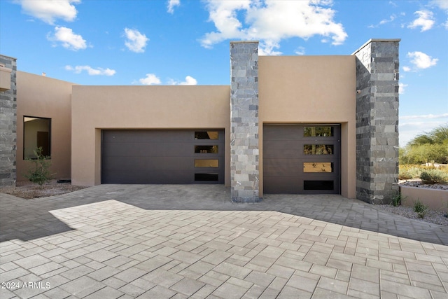 view of front facade with a garage, decorative driveway, a chimney, and stucco siding