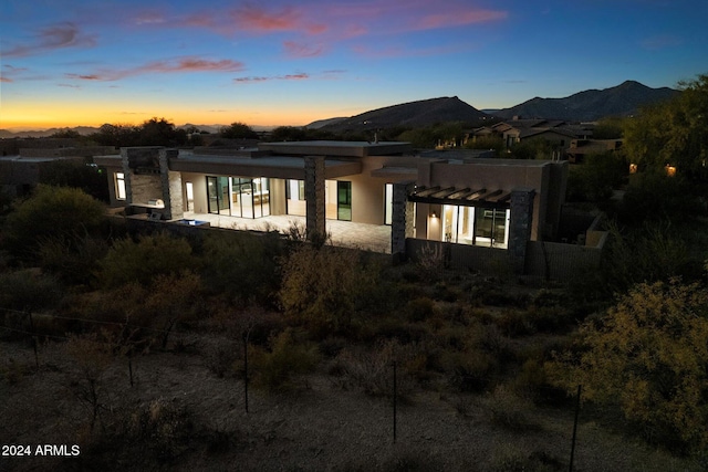 back of house at dusk featuring a mountain view and stucco siding