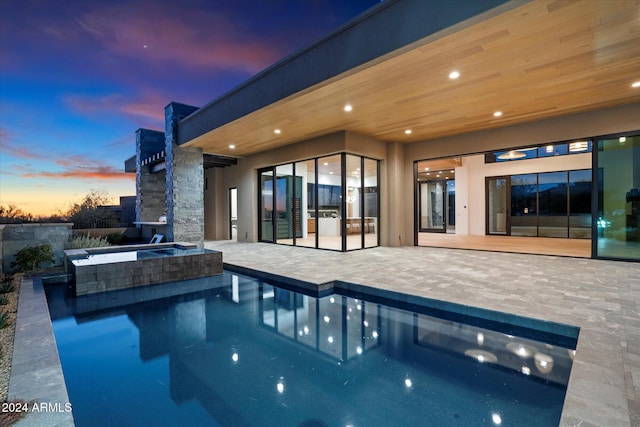 pool at dusk with an in ground hot tub, an outdoor pool, and a patio