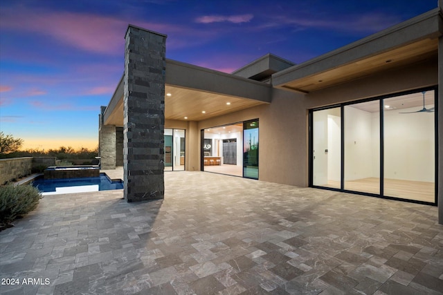 patio terrace at dusk featuring a ceiling fan and an outdoor pool