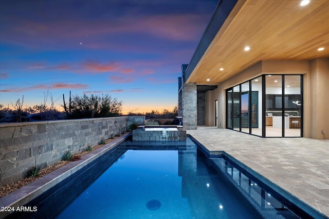 pool at dusk featuring an in ground hot tub and a patio