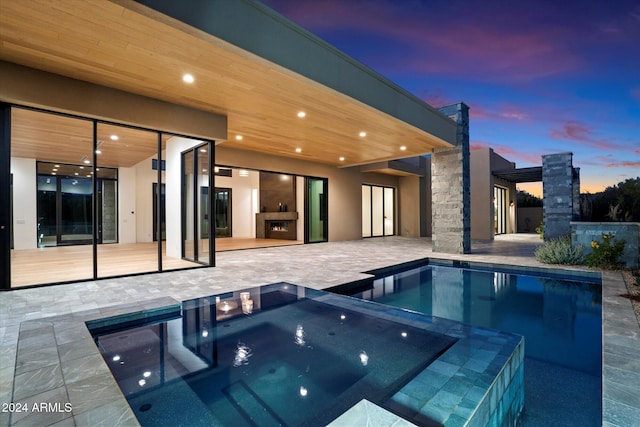 pool at dusk featuring an in ground hot tub, a patio area, and an outdoor fireplace