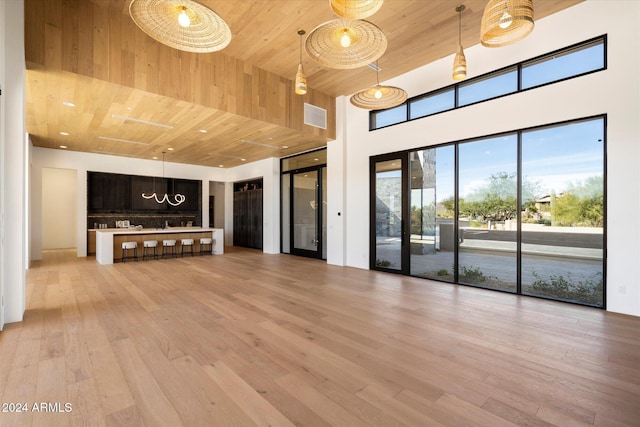 unfurnished living room featuring light wood-type flooring, wooden ceiling, visible vents, and a high ceiling