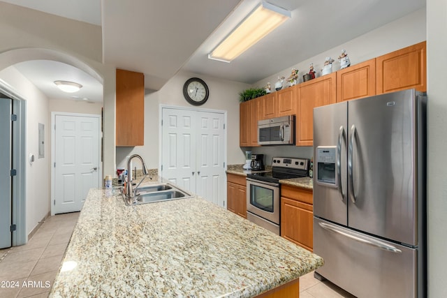 kitchen featuring light tile patterned flooring, appliances with stainless steel finishes, light stone counters, and sink