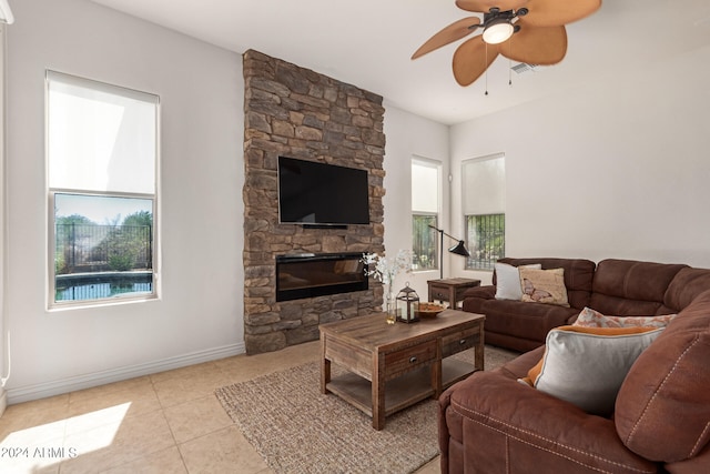 living room featuring ceiling fan, light tile patterned flooring, and a stone fireplace