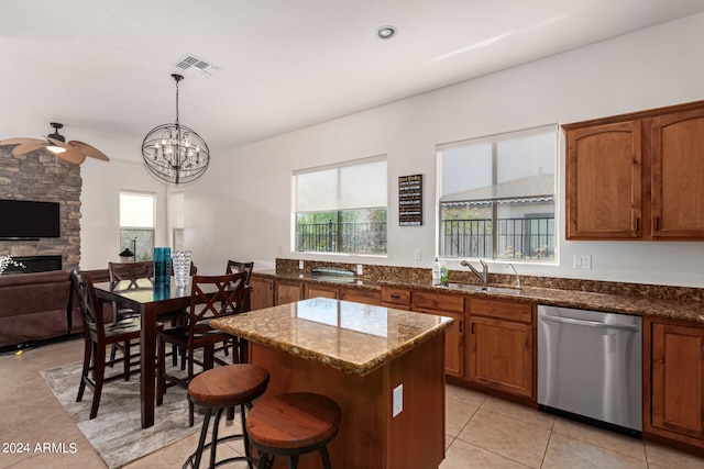 kitchen with hanging light fixtures, ceiling fan with notable chandelier, dishwasher, sink, and a stone fireplace