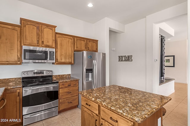 kitchen with dark stone countertops, appliances with stainless steel finishes, light tile patterned floors, and a center island