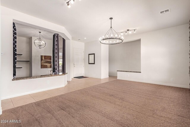 empty room with light carpet, a chandelier, and track lighting