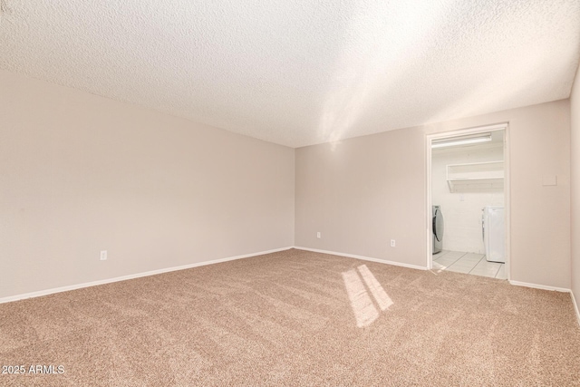 empty room with washing machine and dryer, light carpet, a textured ceiling, and baseboards