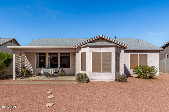 view of front facade featuring stucco siding, roof with shingles, and a patio