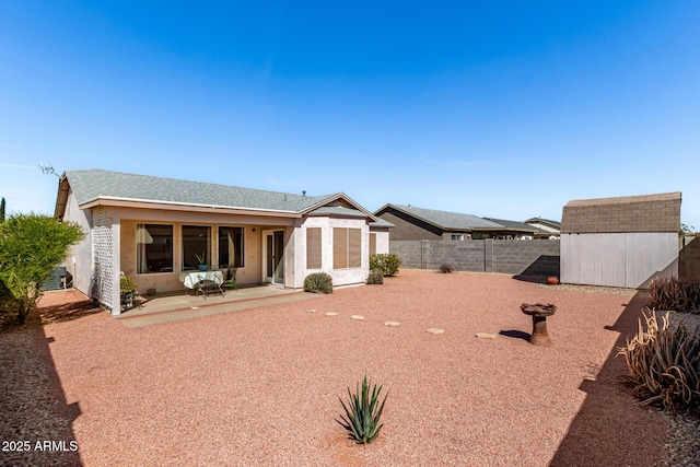 view of front facade with a patio, a fenced backyard, a storage shed, a shingled roof, and an outdoor structure