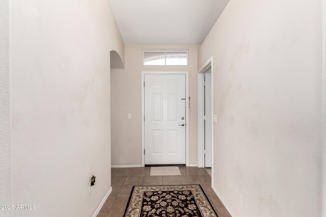 doorway to outside featuring tile patterned flooring, arched walkways, and baseboards