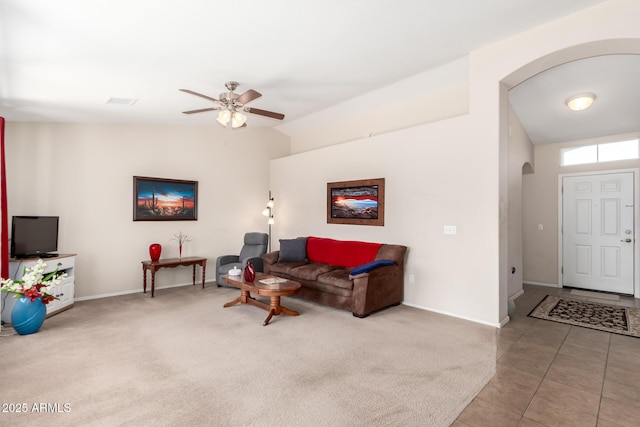 carpeted living room with arched walkways, lofted ceiling, a ceiling fan, baseboards, and tile patterned floors