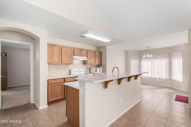 kitchen featuring light tile patterned floors, under cabinet range hood, white appliances, light countertops, and decorative backsplash