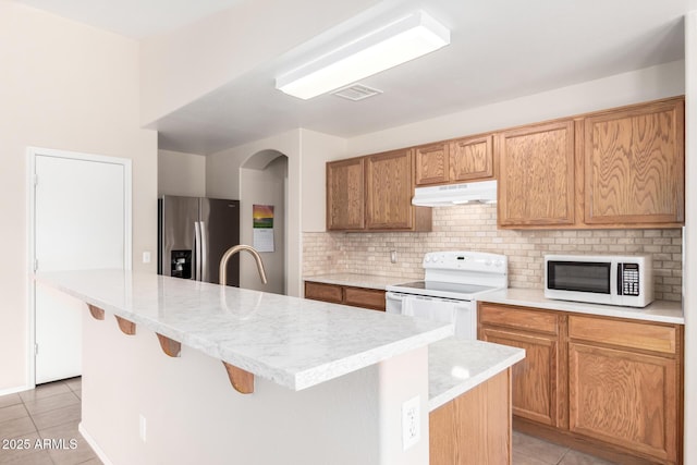 kitchen with white appliances, light tile patterned flooring, visible vents, and under cabinet range hood