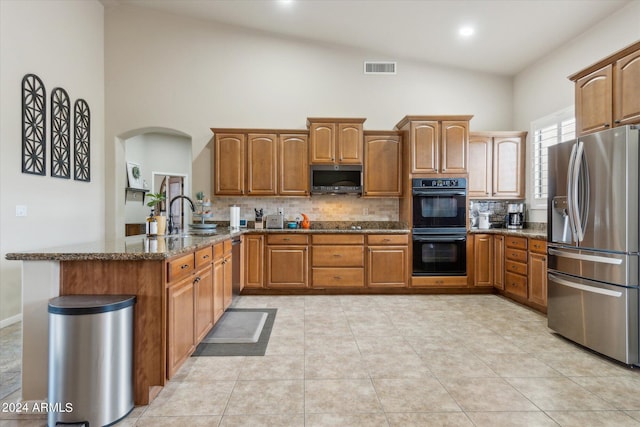 kitchen with dark stone counters, high vaulted ceiling, stainless steel appliances, kitchen peninsula, and sink