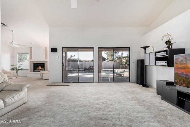 living room with ceiling fan, a tile fireplace, light carpet, and high vaulted ceiling