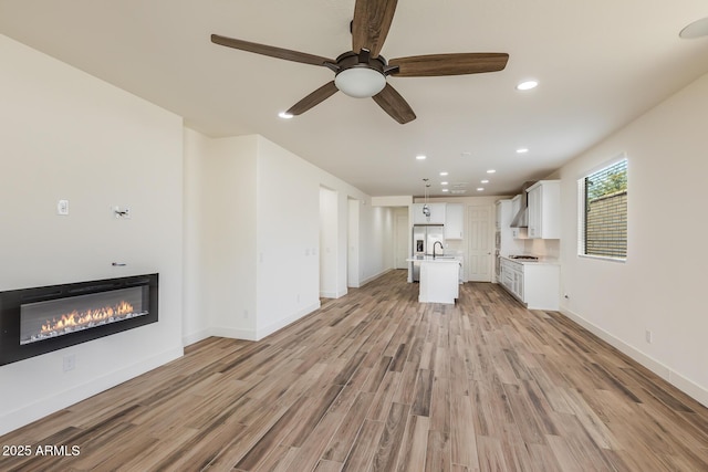 unfurnished living room featuring baseboards, ceiling fan, light wood-type flooring, recessed lighting, and a glass covered fireplace