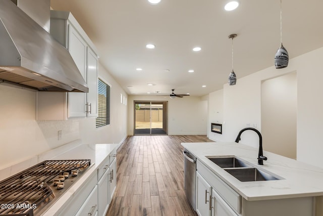 kitchen featuring ceiling fan, light wood-style flooring, appliances with stainless steel finishes, wall chimney exhaust hood, and a sink