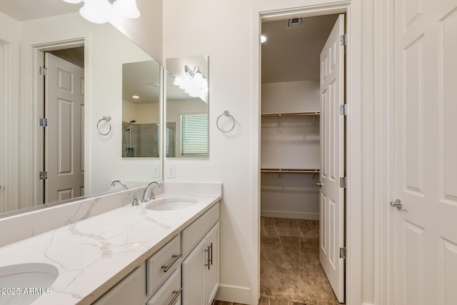 bathroom featuring visible vents, a walk in closet, double vanity, a stall shower, and a sink