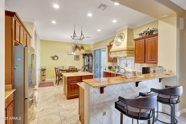 kitchen with kitchen peninsula, hanging light fixtures, custom range hood, a kitchen bar, and high end refrigerator