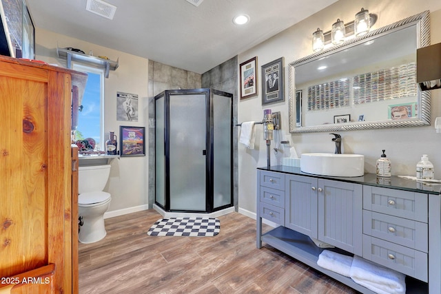 bathroom with hardwood / wood-style floors, toilet, a shower with shower door, and vanity