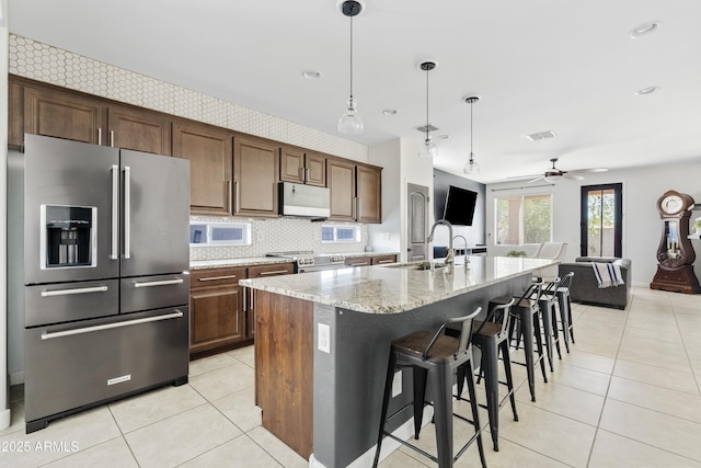 kitchen featuring light tile patterned floors, light stone counters, a kitchen breakfast bar, stainless steel appliances, and a sink