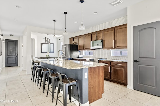 kitchen with visible vents, light stone countertops, light tile patterned floors, stainless steel appliances, and a kitchen island with sink