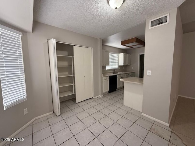 kitchen featuring dishwasher, sink, white cabinets, light tile patterned floors, and a textured ceiling