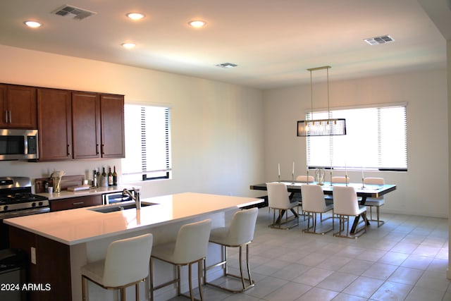 kitchen featuring appliances with stainless steel finishes, sink, an island with sink, hanging light fixtures, and light tile patterned flooring