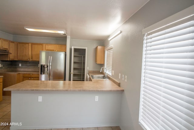 kitchen featuring backsplash, light tile patterned floors, sink, stainless steel fridge, and kitchen peninsula