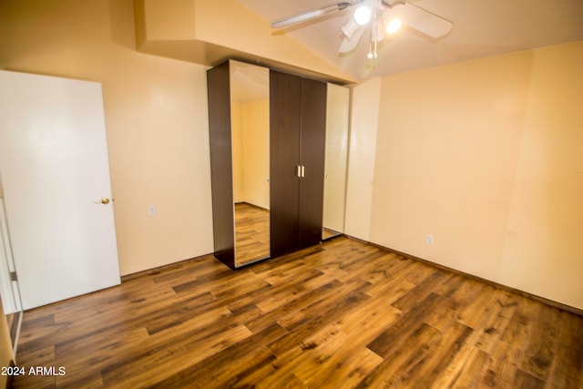 unfurnished bedroom featuring lofted ceiling, a closet, wood-type flooring, and ceiling fan