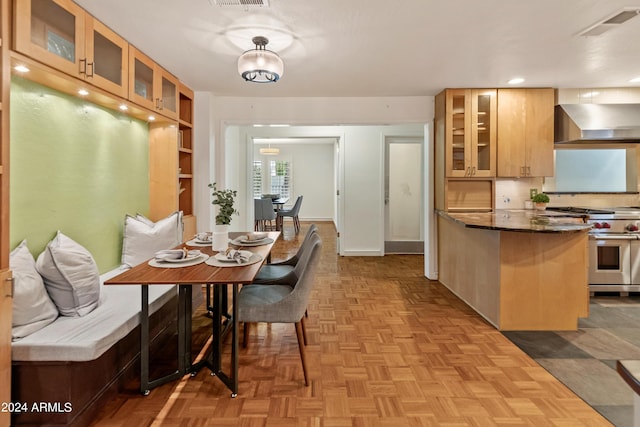 kitchen with kitchen peninsula, dark stone counters, luxury range, light parquet floors, and wall chimney range hood