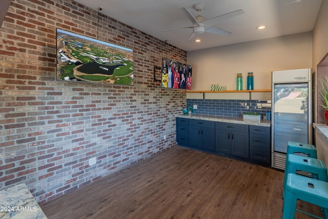 kitchen with built in fridge, light stone counters, dark wood-type flooring, and brick wall