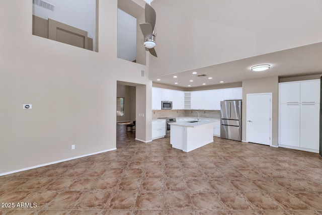 kitchen with appliances with stainless steel finishes, backsplash, white cabinets, a high ceiling, and a center island